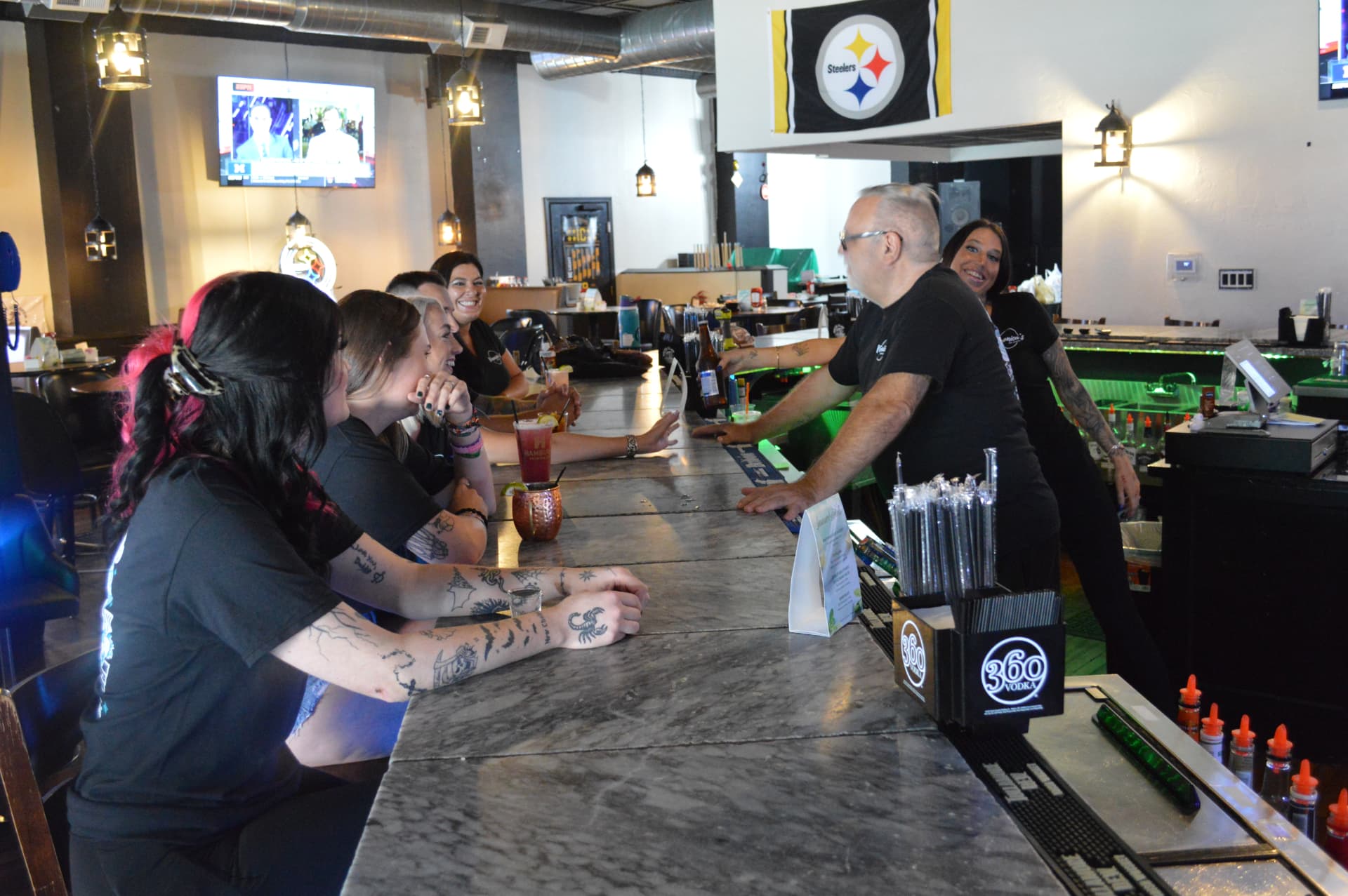 Ron leaning across the bar in conversation with guests while the hospitality team keeps service moving